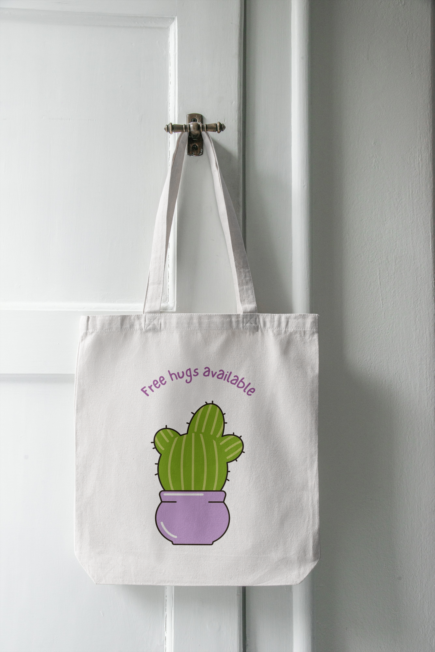 Tote bag with a cactus design and 'Free hugs available' text hanging on a white door.