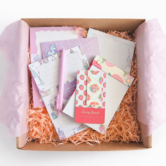 Box of stationery items including notebooks, notepads, holographic magnetic bookmark and pen on a white background