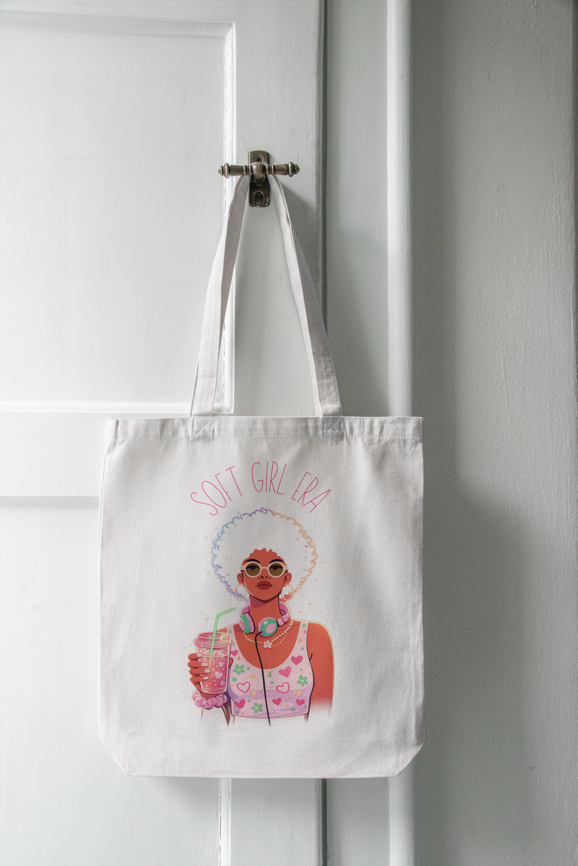 Tote bag with a graphic design of a woman and 'Soft Girl Era' text, hanging on a white door.