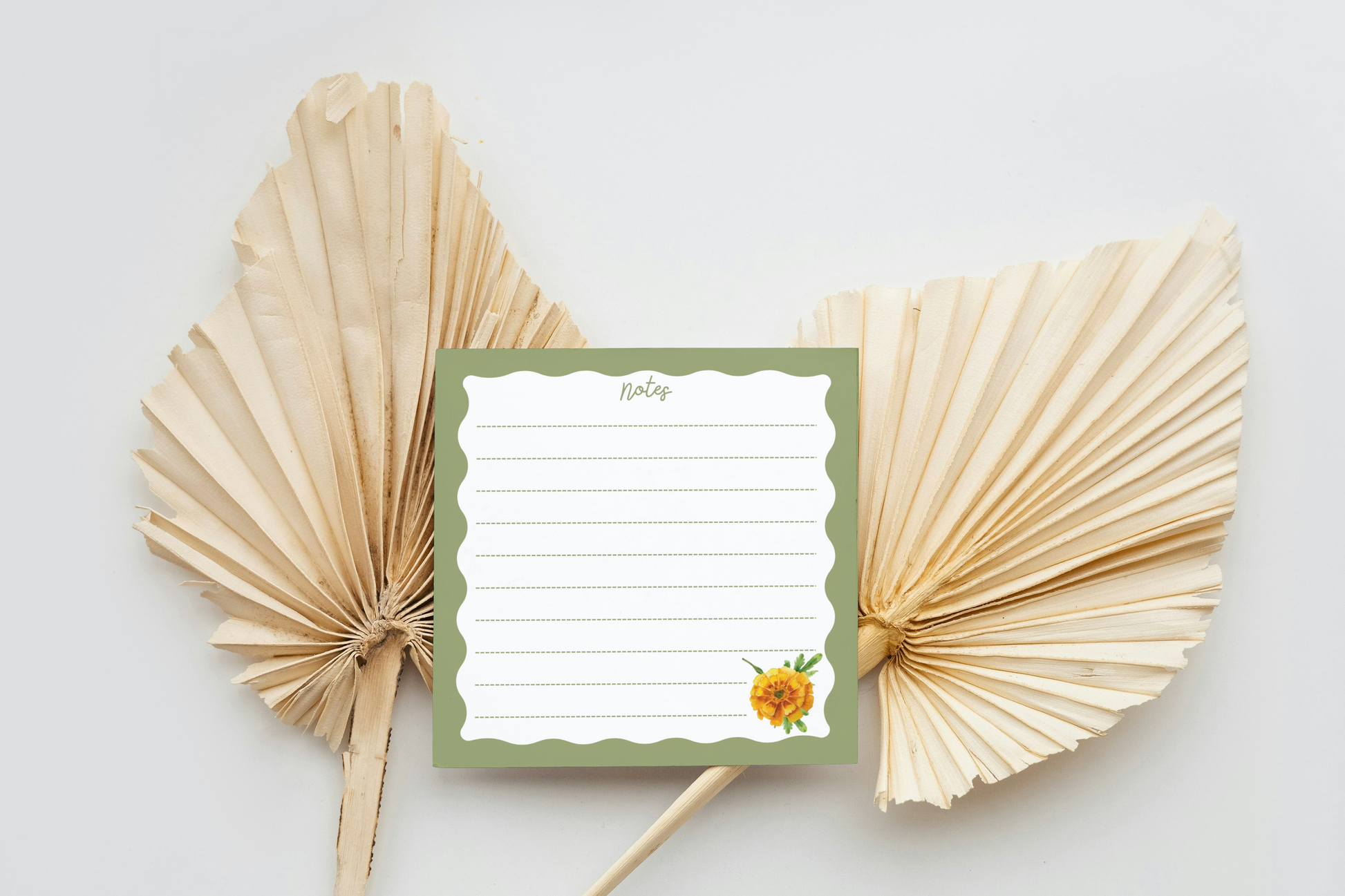 Memo pad with a flower design on a white background with decorative dried leaves.