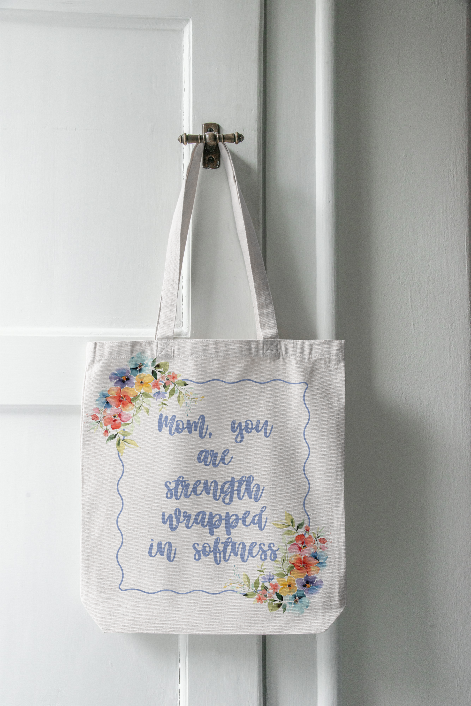 Tote bag with floral design and text hanging on a door handle.