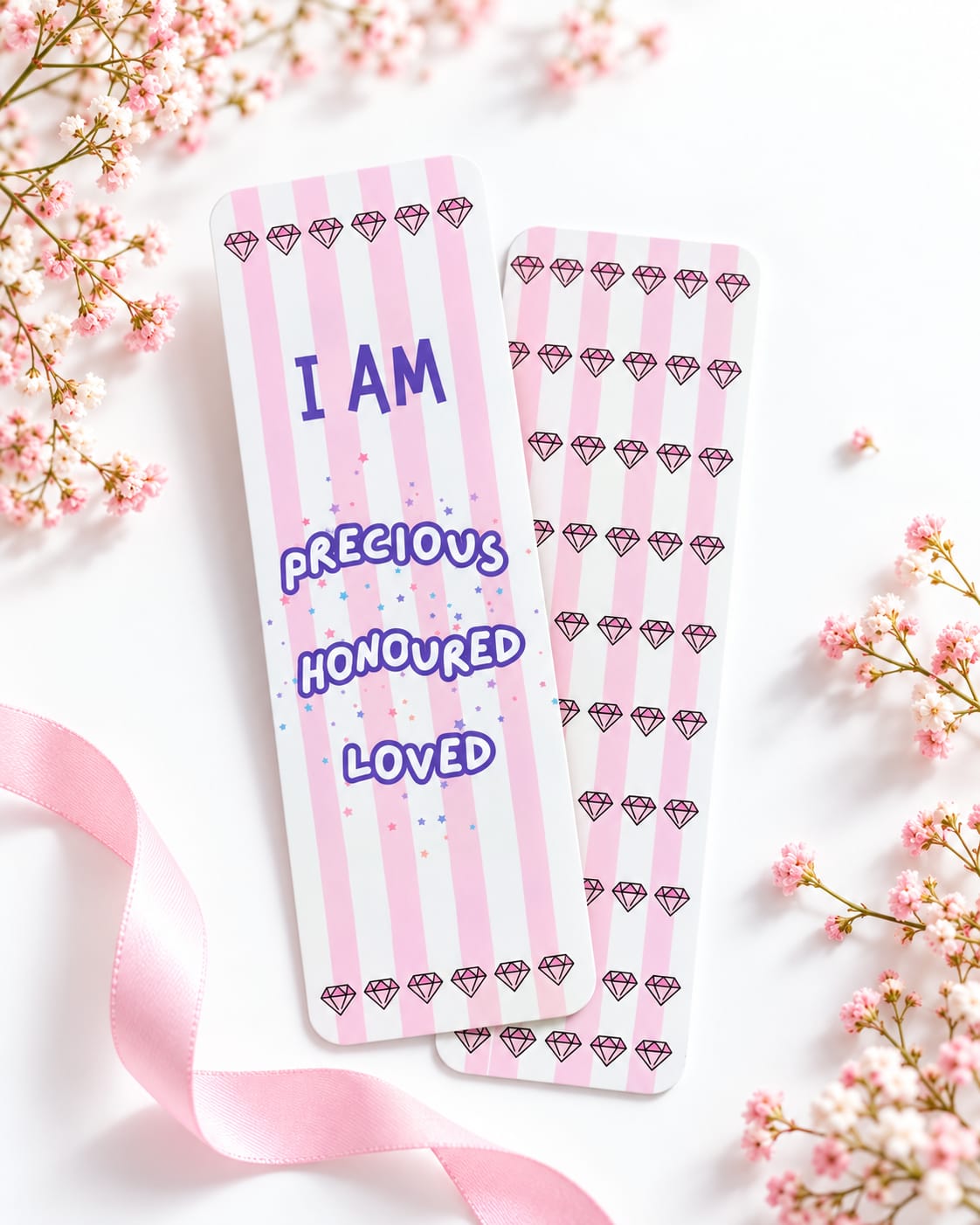 Two pink striped bookmarks with purple text and diamond patterns, styled on a white surface with pink flowers and a ribbon.