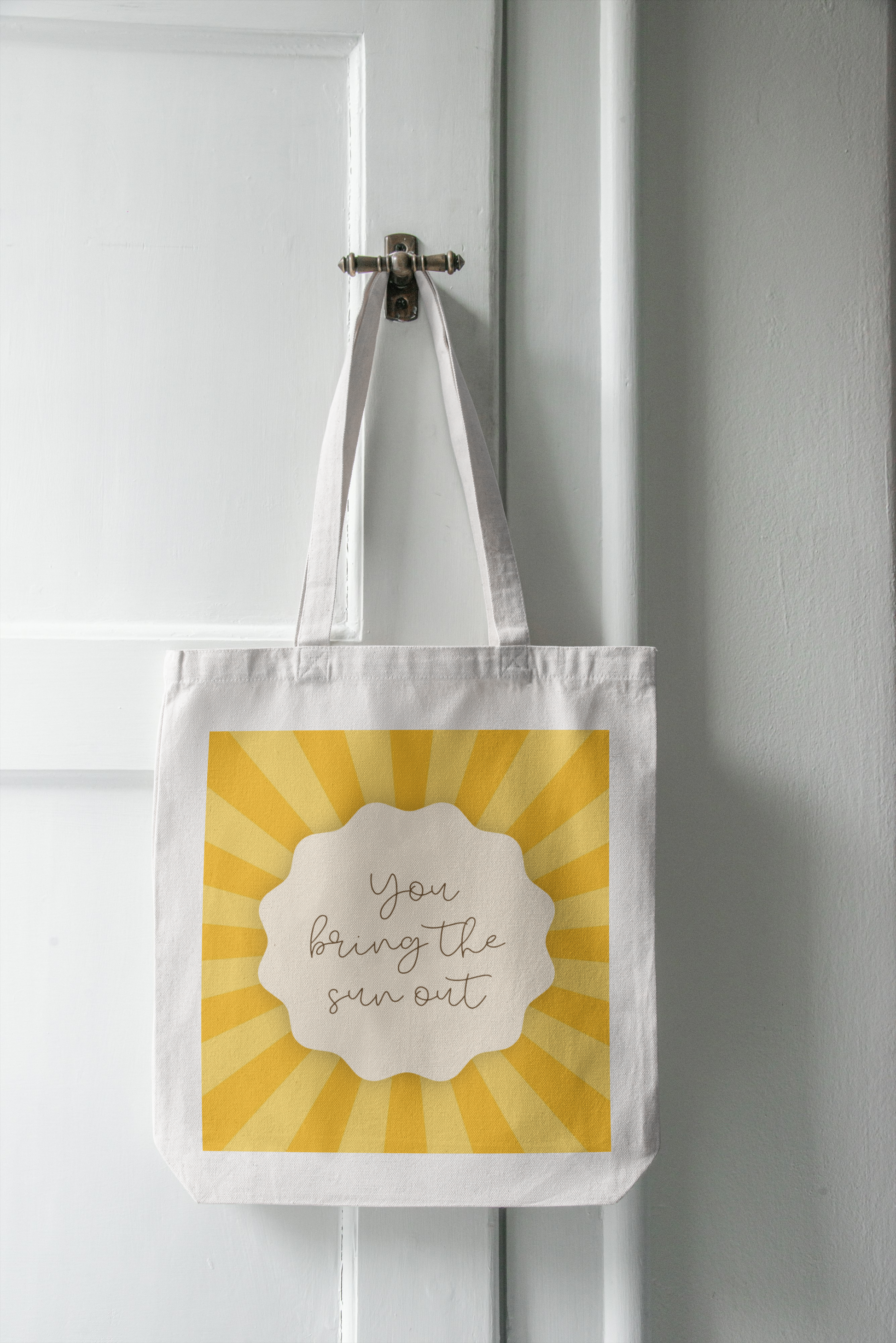 Tote bag with a sun design and text hanging on a white door.