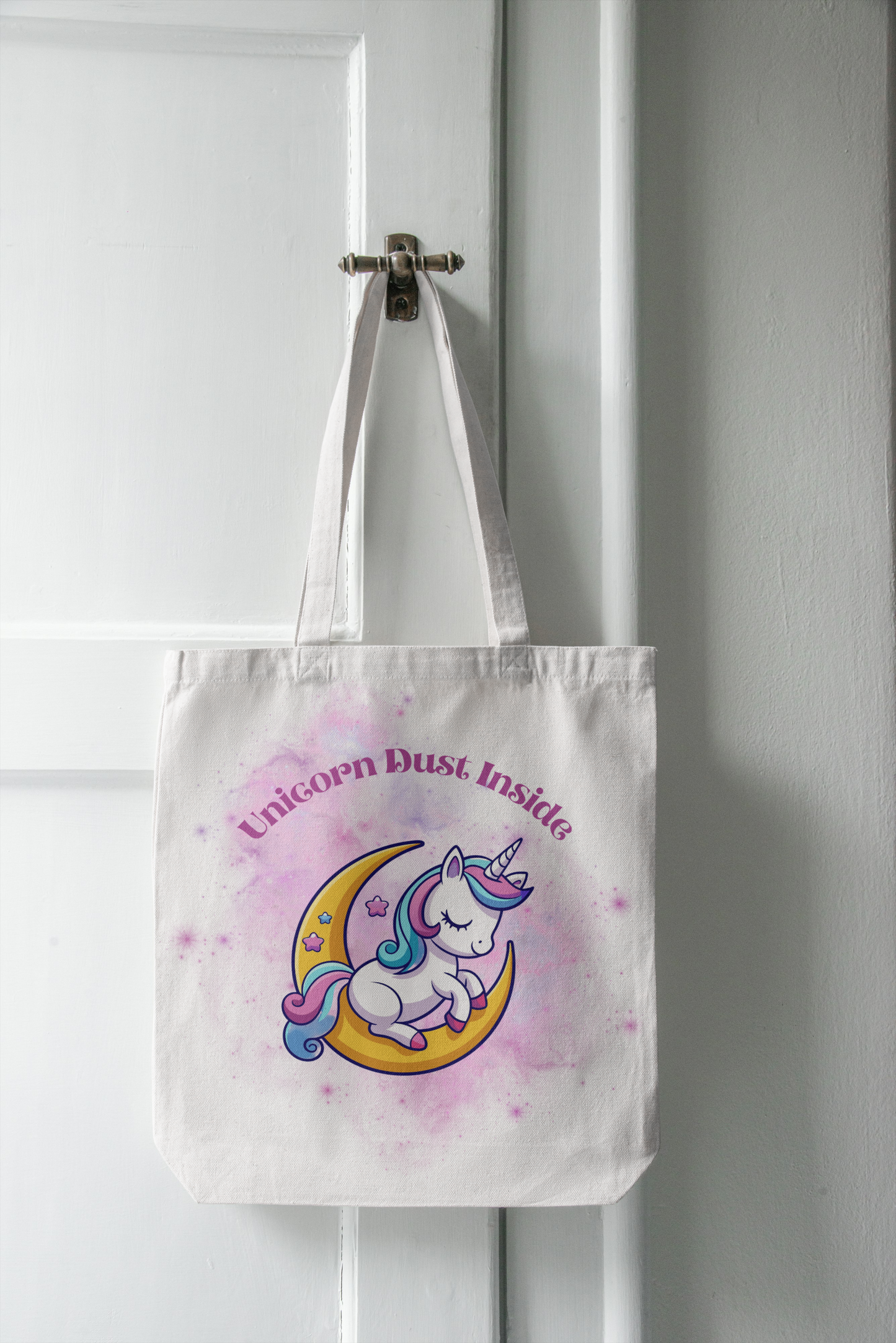 Tote bag with unicorn design and 'Unicorn Dust Inside' text hanging on a white door.